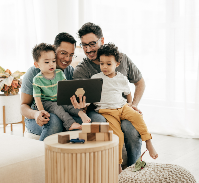 A family smiles while watching something on their table, with the two young children sitting on their parents lap.