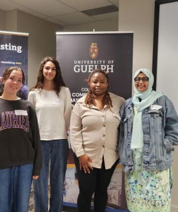 A group of competitors at the datathon standing infront of UofG banners. Zach Ribau is featured on the left side